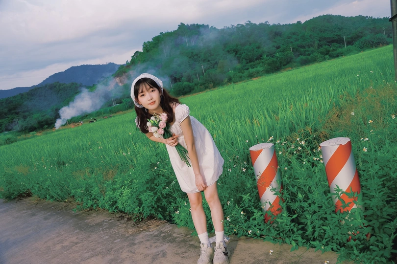 一位穿着白色连衣裙的年轻女子站在绿色的原野上