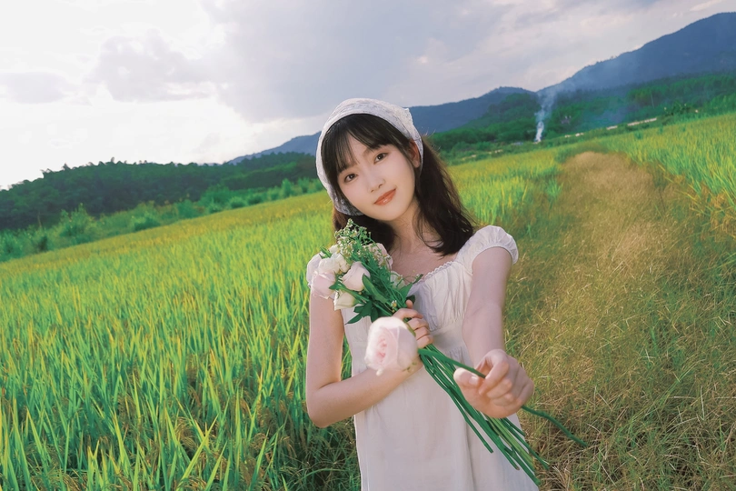 一个小女孩穿着白色裙子 手里拿着一束花 站在绿色的草地上。