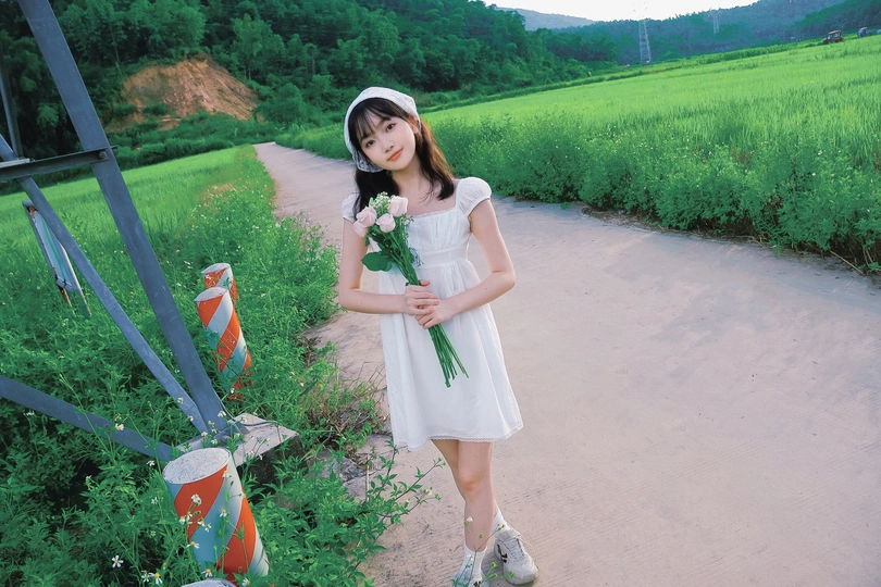 一个小女孩穿着白色连衣裙站在一条小径旁边的一个田地