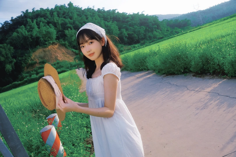 一位穿着白色连衣裙的年轻女子站在公路上 拿着网球拍。