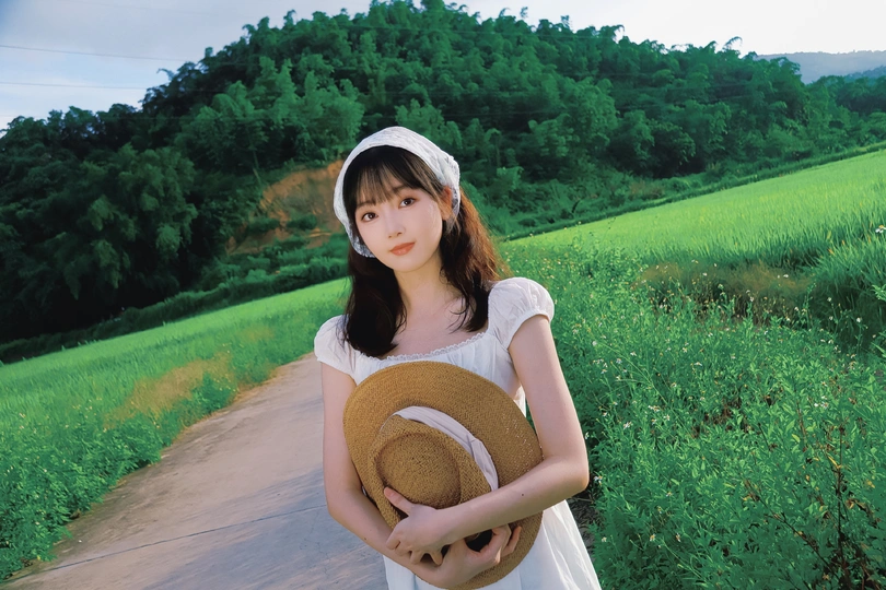 一个小女孩穿着白色裙子 戴着草帽站在公路上。