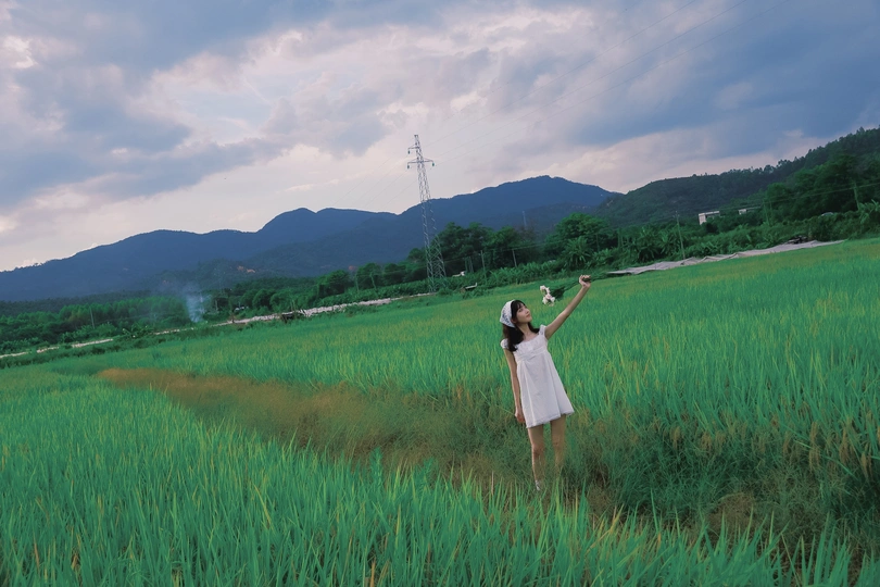 一位穿着白色连衣裙的女士站在一片绿色的草地上 背景是山脉。