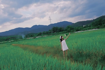一位穿着白色连衣裙的女士站在一片绿色的草地上 背景是山脉。