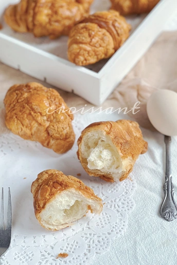 桌子上的一个白色盘子 里面有一些羊角面包、一个鸡蛋和一把叉子