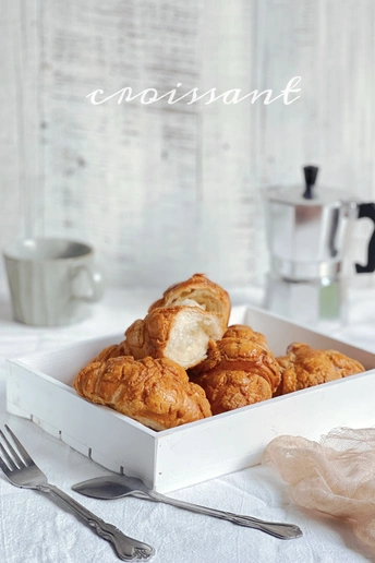 桌子上放着一个装满羊角面包的白色盘子 旁边放着一杯咖啡和一把叉子