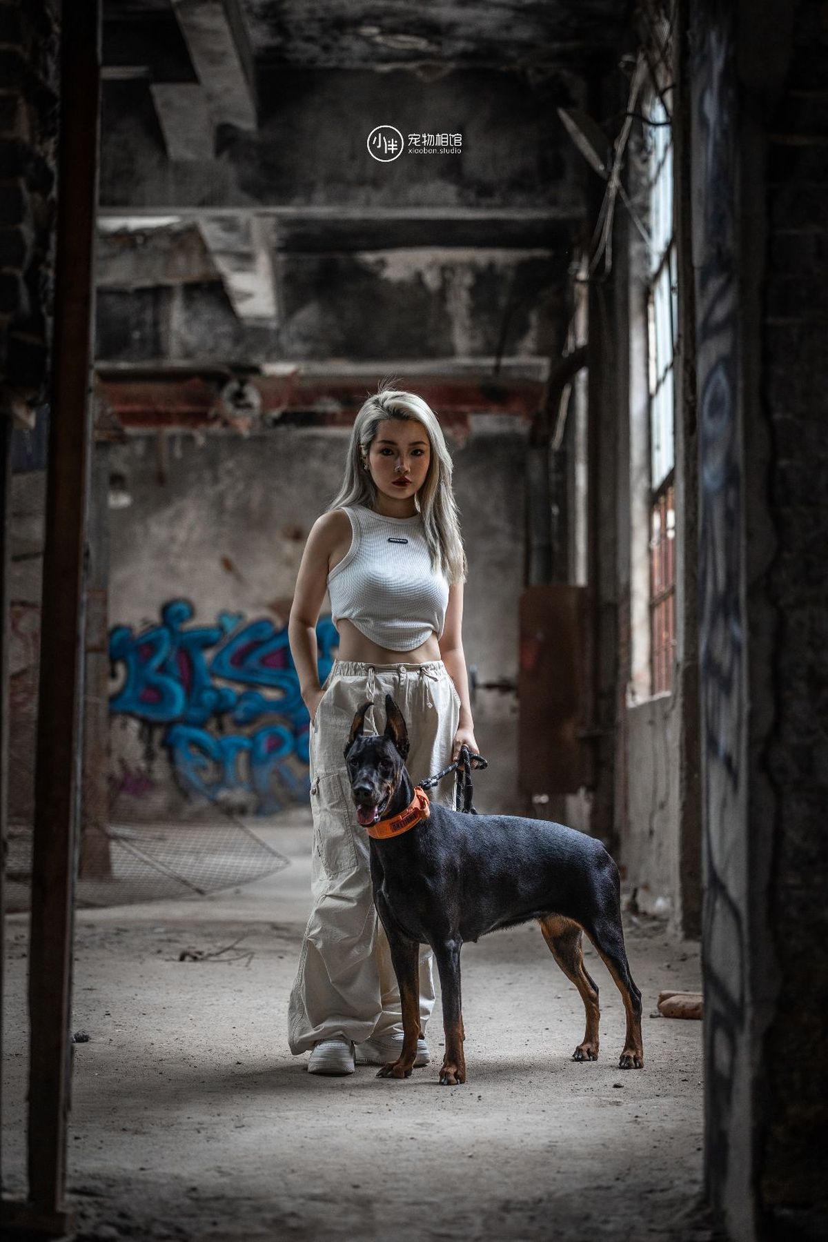 一个穿着连衣裙的女人站在一个废弃的仓库里带着一只狗