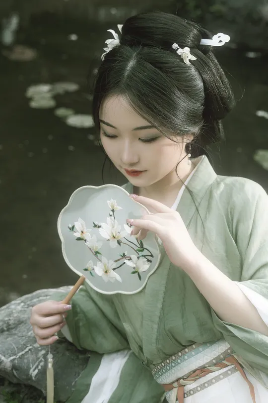 一位穿着绿色连衣裙的年轻女子在水边拿着白色花朵