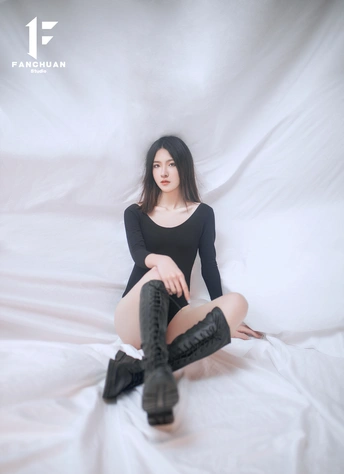 一位穿着黑色靴子的孕妇坐在铺着白色床单的床上摆姿势拍照