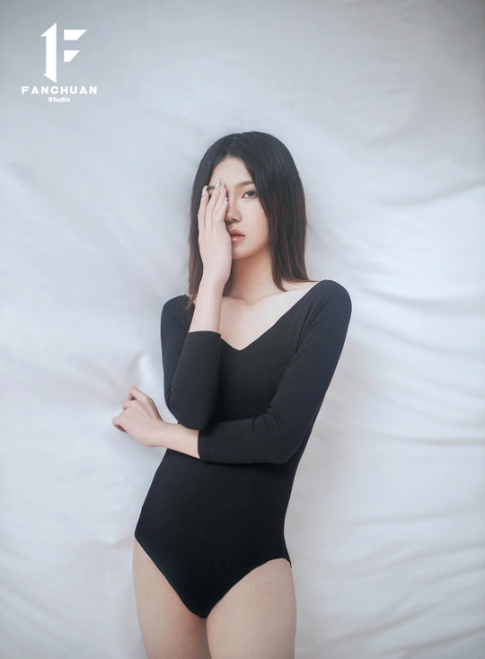 一个穿着黑色衣服的孕妇在铺着白色床单的床上摆姿势