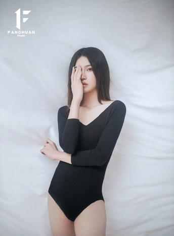 一个穿着黑色衣服的孕妇在铺着白色床单的床上摆姿势