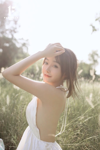 一位美丽的年轻女子穿着一件白色连衣裙站在一片高草地上