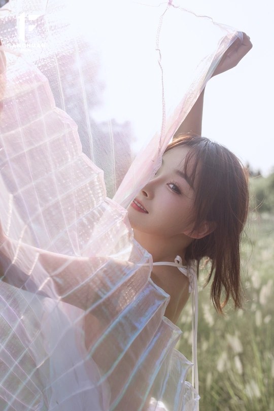 一个穿着白色连衣裙的年轻女子手持雨伞站在田野中 太阳落山了。