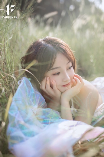 一位穿着漂亮裙子的年轻女孩坐在田野中的 tall grass 中。