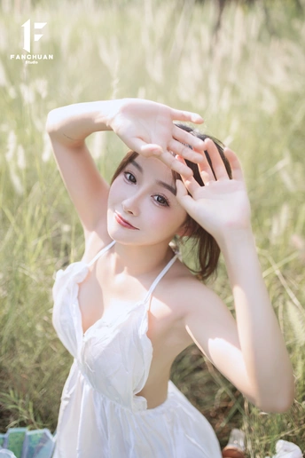 一位美丽的年轻女子穿着白色裙子坐在田野里