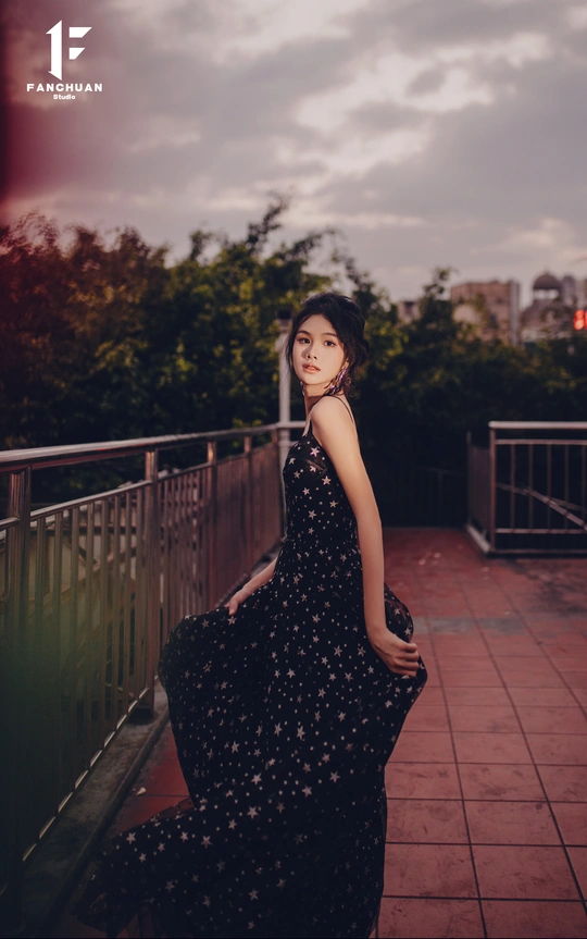 一个穿黑色连衣裙的年轻女子站在阳台上 带着一把雨伞。