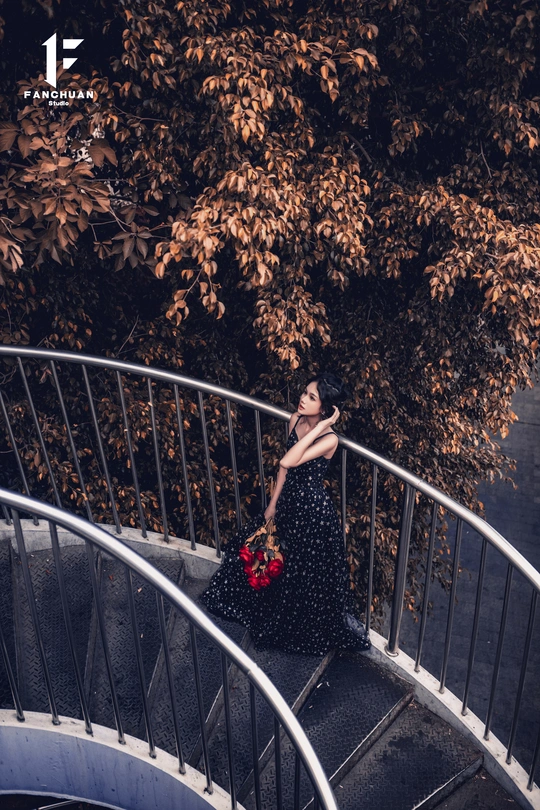 一个穿黑色连衣裙 胸前有红花的女子站在螺旋楼梯上