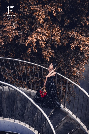 一个穿黑色连衣裙 胸前有红花的女子站在螺旋楼梯上