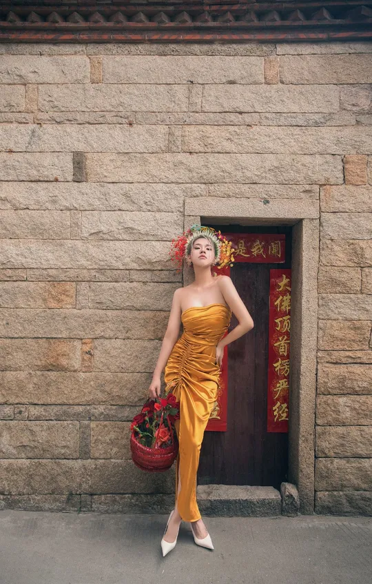 一位穿着黄色连衣裙的女人站在一个有红色篮子的墙壁前