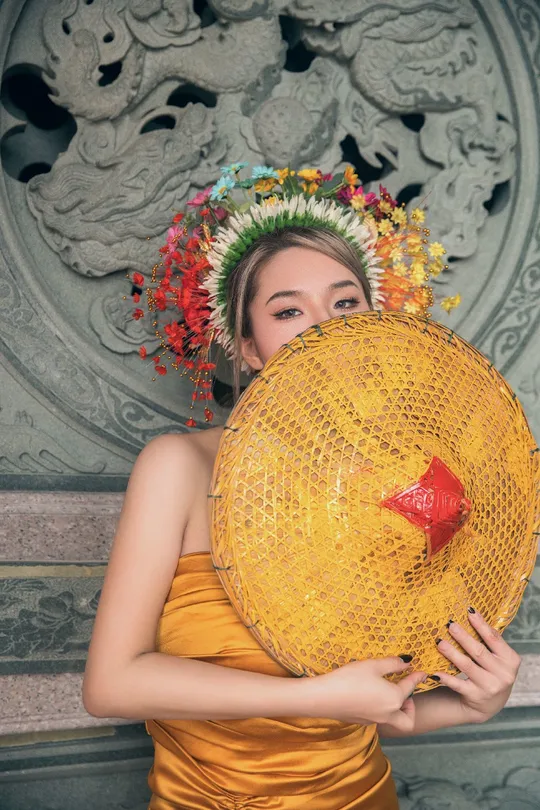 一位穿着黄色连衣裙的女士举着一大顶帽子在头上