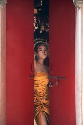 一位穿着黄色连衣裙的年轻女子站在一座红墙和柱子的寺庙中