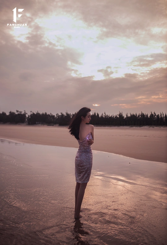 一个穿着漂亮裙子在日落时漫步在海滩上的年轻女子
