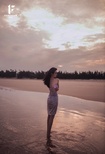 一个穿着漂亮裙子在日落时漫步在海滩上的年轻女子