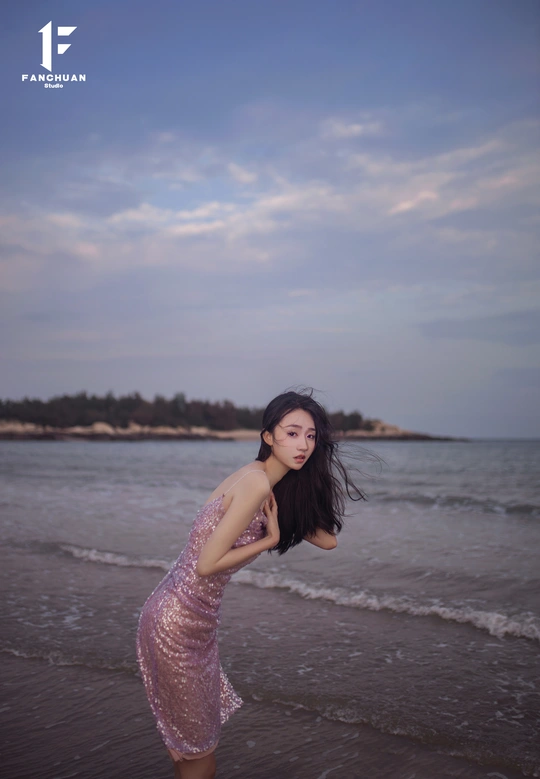 一个穿着粉色连衣裙的美丽年轻女子站在海滩的水中