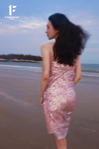 一位穿着粉红色连衣裙的年轻女子在靠近海洋的海滩上行走。