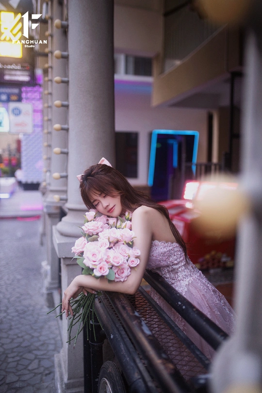 一个穿着漂亮裙子 手里拿着粉色玫瑰花束 坐在长凳上的年轻女子。