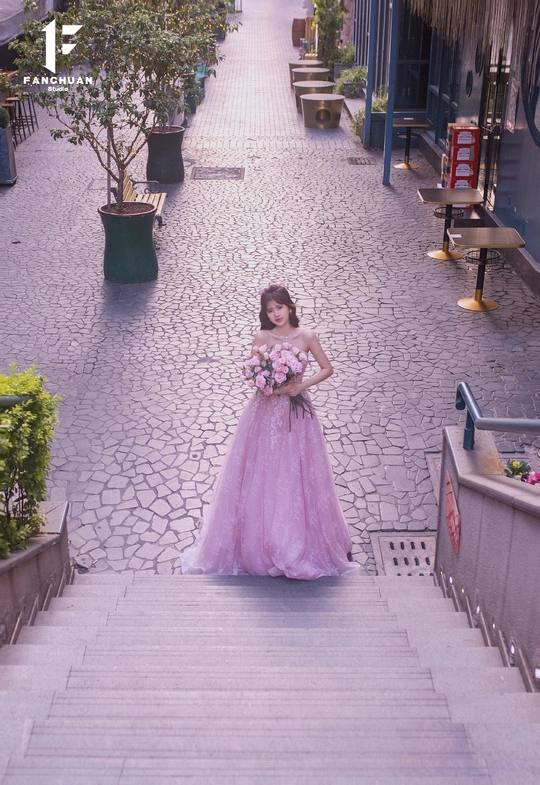 一位穿着紫色长裙 裙尾拖地的美丽年轻女子站在街道的台阶上 俯视着街道。