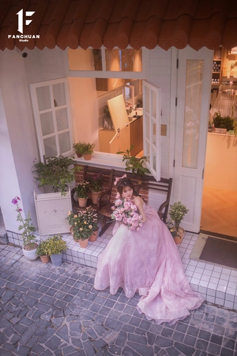 一个穿着粉红色连衣裙的年轻女子坐在长凳上 身着粉红色长袍 手持鲜花。