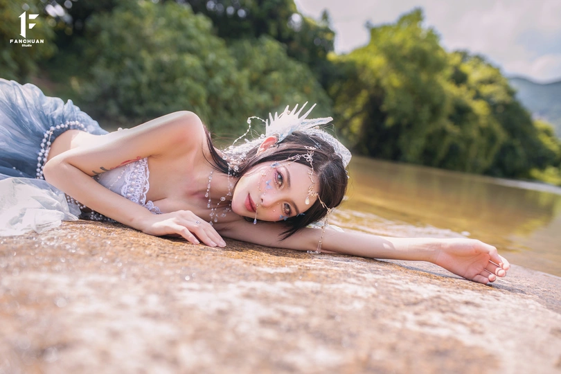 一位穿着美丽裙子的年轻女子躺在河中的岩石上