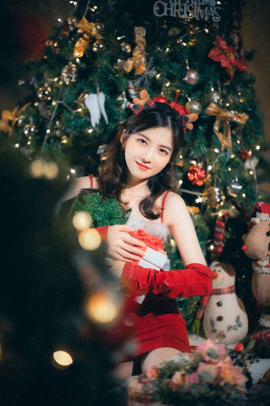 一位穿着红色连衣裙的年轻女子在圣诞树前摆姿势
