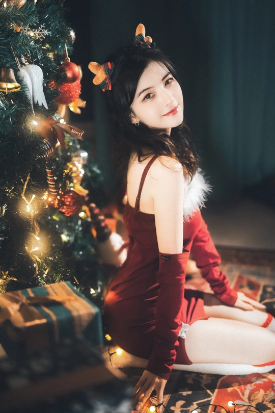 一位穿着红色连衣裙的年轻女子在圣诞树前摆姿势