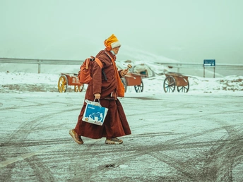 一个穿着僧袍的僧人在雪中行走 走在一条路上。