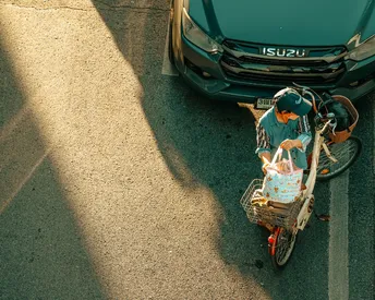 一位男士骑着一辆自行车 旁边停着一辆绿色汽车 车篮里有一个篮子。