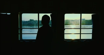 一个黑暗的剪影 一个男子和一个女子在船上 透过窗户看向水面。