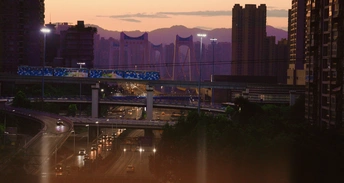 傍晚或日落时的一条城市街道 有高大的建筑和一座有灯光的交通桥。