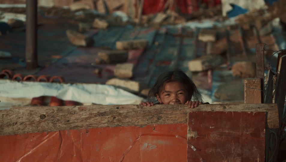 一个女孩坐在瓦砾堆中 另一个孩子在一旁观看。