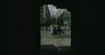 一个黑暗的城市街道 有建筑和一个人骑自行车在街上。