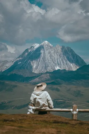 一个人坐在长凳上 前方有围墙 正在凝视一座山脉。