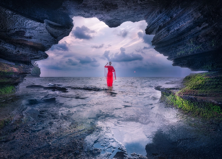 一个人站在海滩上的洞穴里 凝视着海洋中的红灯塔。