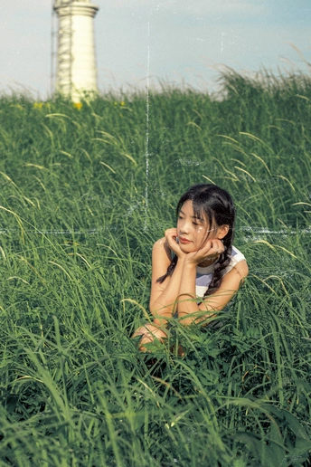 一个小女孩坐在一片高草地上 背景中有灯塔。
