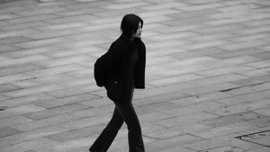一张黑白照片 照片中一名年轻女子走在人行道上 一名男子在她身后