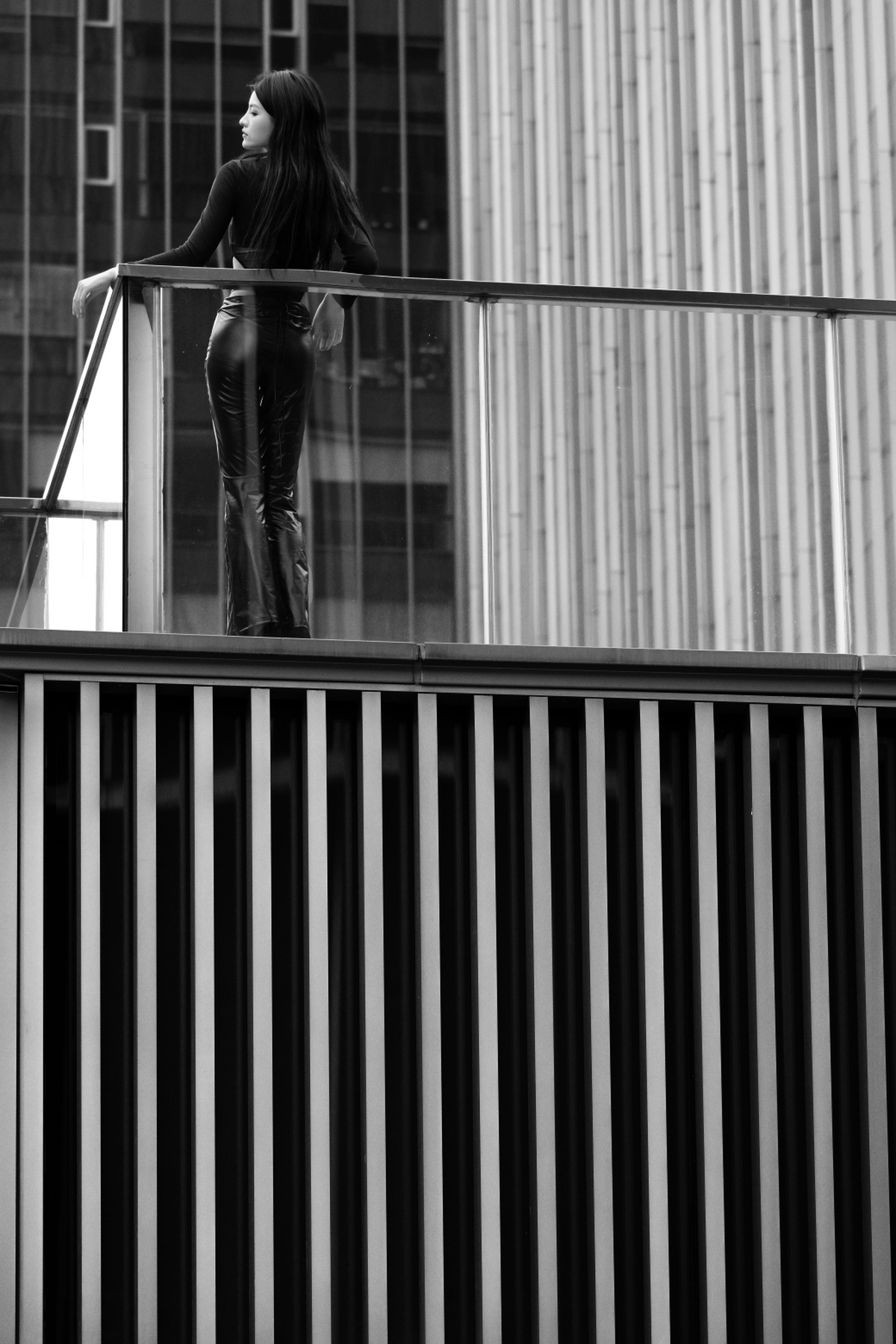一个女孩站在阳台上 靠在栏杆上 背景是高楼大厦