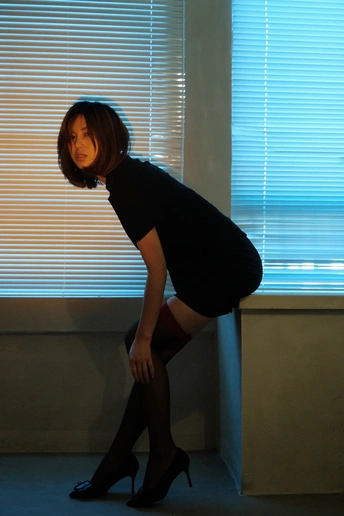 一位穿着高跟鞋和黑色鞋子的年轻女子靠在一间房间的窗户旁