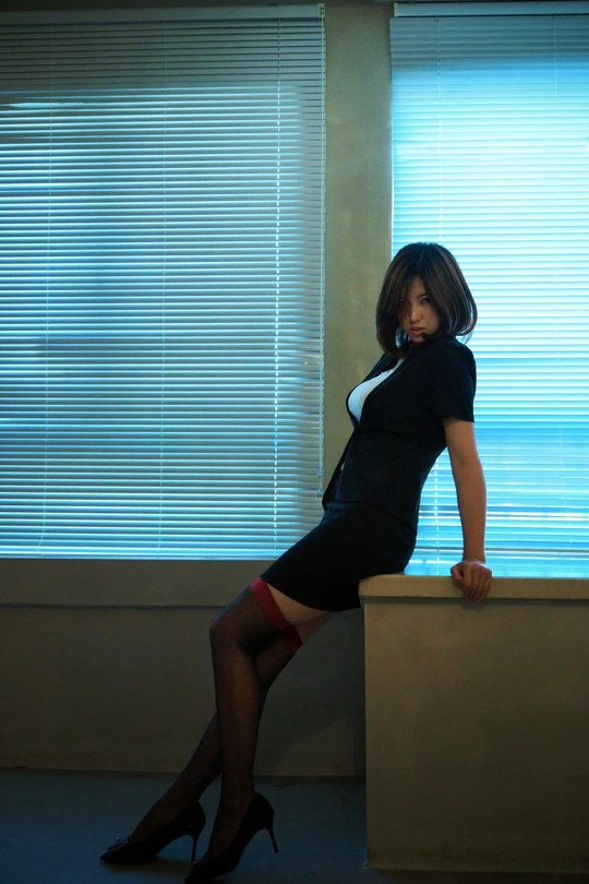 一位穿着短黑裙和高跟鞋的年轻女子在房间的窗户前摆姿势