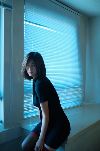 一个年轻女子坐在窗台上 房间的百叶窗拉下了。