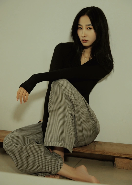 一个年轻女子穿着黑色裙子坐在地板上的长凳上