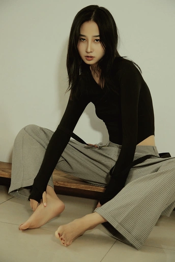 一个穿着黑色裙子和黑色裤子的年轻女子坐在地板上 双腿交叉。